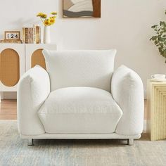 a white chair sitting in a living room next to a vase with flowers on it