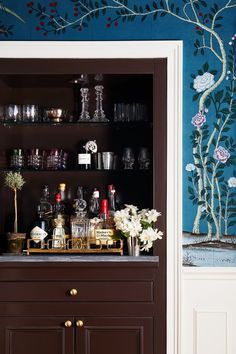 a cabinet with liquor bottles and glasses on it in front of a wallpapered wall