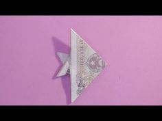 an origami bird made out of money on a pink wall with purple background