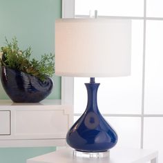 a blue vase sitting on top of a white table next to a lamp with a green plant in it