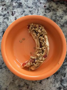 an orange bowl filled with granola and sliced banana on top of a marble counter