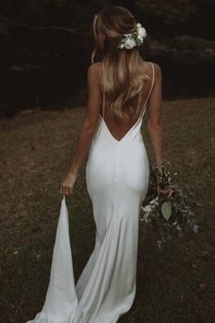 the back of a woman in a white dress holding a bouquet and wearing a flower crown