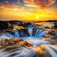 the sun is setting over an ocean with rocks and water flowing down it's sides