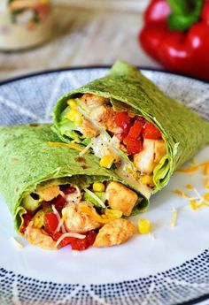 two wraps filled with chicken and vegetables on a white plate next to an orange tomato