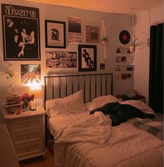 an unmade bed in a bedroom with pictures on the wall above it and a lamp next to it