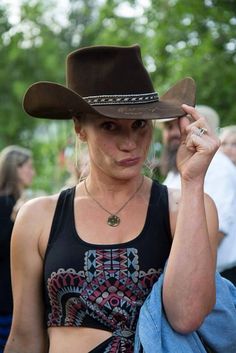 a woman wearing a cowboy hat and holding her hand up to her ear while standing in front of other people