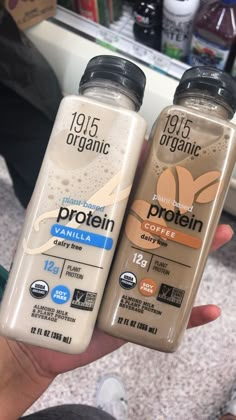 two bottles of protein drink are being held by someone's hand in a store