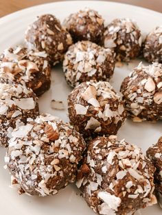 a white plate topped with lots of chocolate truffles covered in coconut flakes