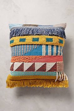 a multicolored pillow with tassels and fringe on the bottom is hanging on a wall