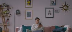 a woman sitting on top of a pink couch holding a cell phone in her hand