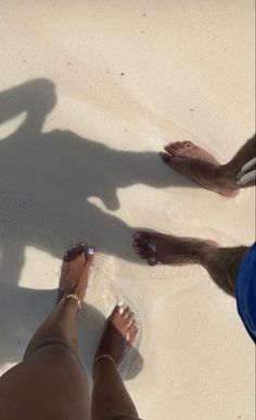 two people standing on the beach with their feet in the sand