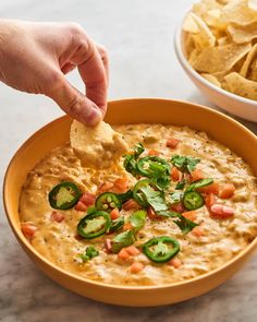 a hand dipping a tortilla chip into a bowl of quesadilla dip