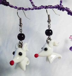 two white dogs with black and red beads hanging from earrings