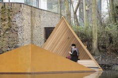 a man sitting on the ground next to a wooden structure with triangular shapes in front of it