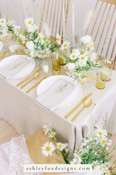 the table is set with white and gold plates, napkins, and daisies