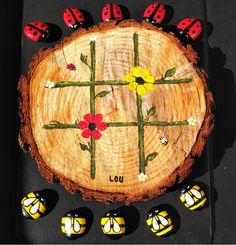 a piece of wood with ladybugs and flowers painted on it, surrounded by small black stones