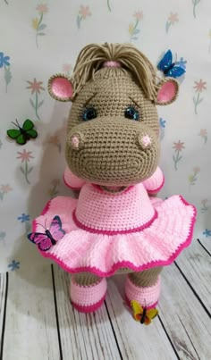 a crocheted stuffed animal in a pink dress with butterflies on the wall behind it