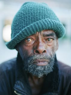 a man with a green hat on his head looking at the camera while wearing a black jacket