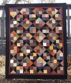 a quilt hanging on a fence in the fall with leaves around it and trees in the background