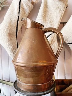 a copper pitcher sitting on top of a stove next to towels and other items in the background