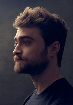 a man with a beard and blue eyes looks off into the distance while standing in front of a dark background