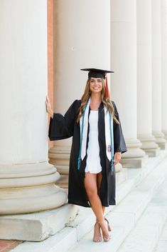 a woman wearing a graduation cap and gown posing for a photo in front of columns