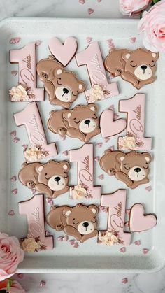 decorated cookies with teddy bears and hearts on a tray next to pink flowers, roses and petals