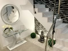 a glass table sitting under a stair case next to a mirror and vase with flowers