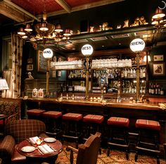 a dimly lit bar with red upholstered chairs and tables in front of it