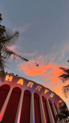 an airplane is flying over the harraks sign and palm trees in front of it