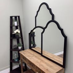 a mirror sitting on top of a wooden dresser next to a shelf filled with flowers