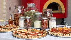 several pizzas and spices on a table