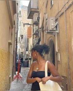 a woman is walking down an alleyway carrying a white bag and looking at her cell phone