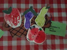 four handprinted fruits are sitting on a checkered tablecloth