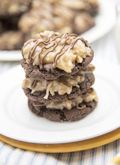 three cookies with chocolate frosting and caramel drizzled on top are stacked on a white plate