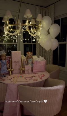 two dolls are sitting at the table with balloons in front of them and a chandelier hanging from the ceiling