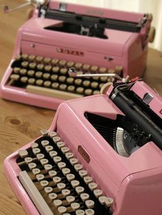 two pink typewriters sitting on top of a wooden table