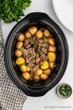 a slow cooker filled with meat and potatoes next to some parsley on the side