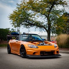 an orange sports car parked in front of a tree