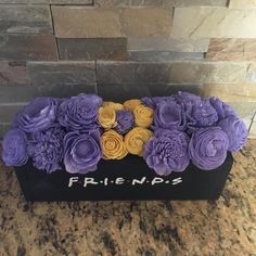 a black box filled with purple and yellow flowers on top of a marble countertop