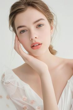 a woman in a white dress with her hand on her chin and looking at the camera