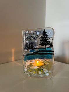 a small glass block with trees and snow on it, sitting on top of a table