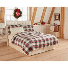 a bed with plaid comforter and pillows in a room filled with wooden floors, white walls