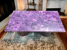 a purple marble table sitting on top of a rug in front of a fire place