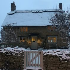 a stone house covered in snow next to a white fence