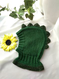 a green knitted mitt next to a yellow sunflower on a white sheet