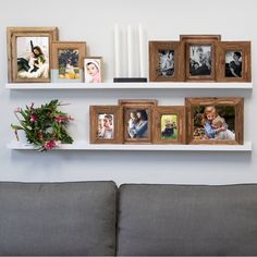 a wall shelf filled with pictures and candles on top of a couch next to a gray sofa