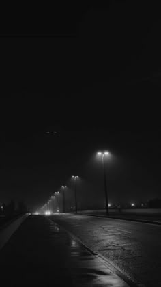 an empty road at night with street lights on the side and dark sky in the background