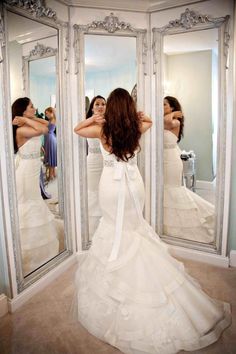 a woman standing in front of a mirror wearing a wedding dress