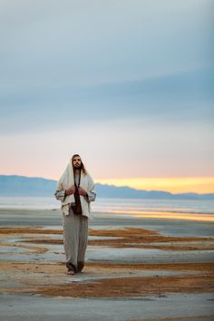 a man with long hair and beard standing in front of the ocean wearing a white robe